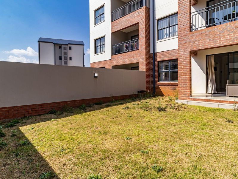 A ground floor apartment unit featuring a private garden area, brick facade, and a covered patio accessible via sliding glass doors.