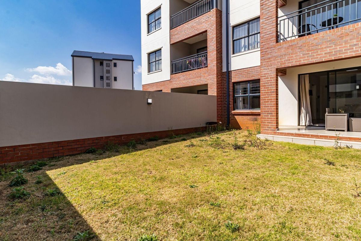 A ground floor apartment unit featuring a private garden area, brick facade, and a covered patio accessible via sliding glass doors.