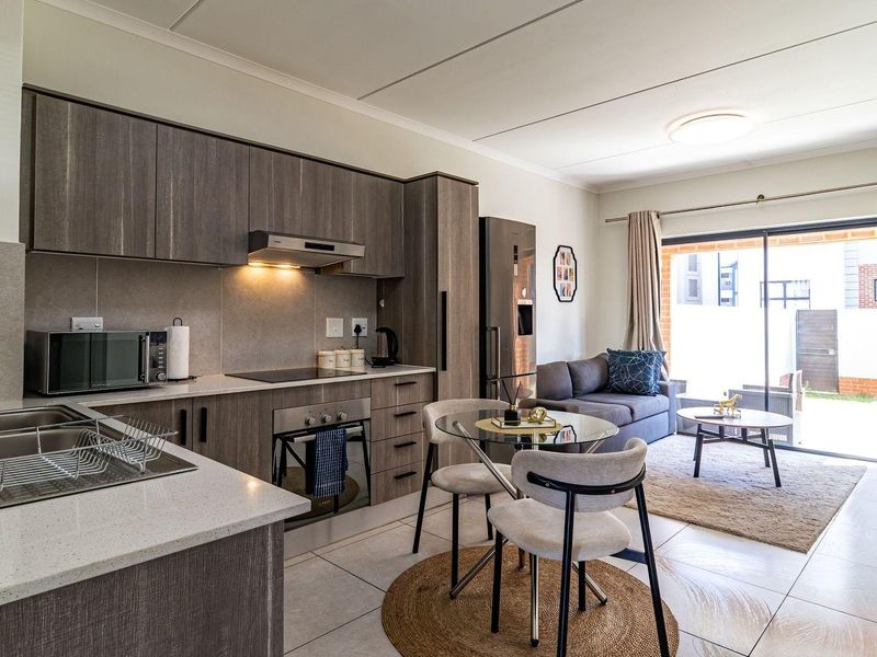 Modern open-plan kitchen and living area featuring contemporary cabinetry, stone countertops, integrated appliances, and direct access to an outdoor patio through sliding glass doors.