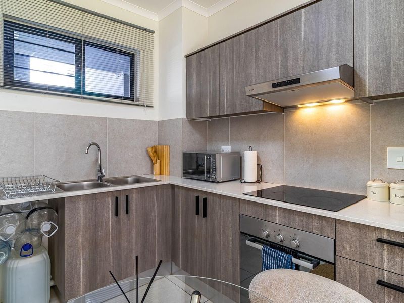 Modern kitchen featuring wood-grain cabinetry, stone countertops, integrated stainless steel appliances, and a tiled splashback with ample storage space.