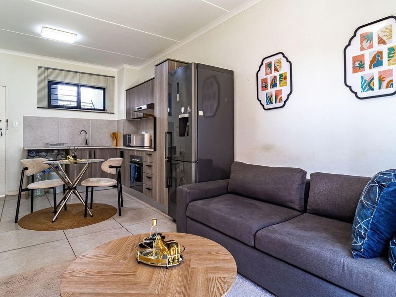 Modern open-plan living area featuring a compact, well-appointed kitchen with built-in cabinetry and tiled flooring, seamlessly integrated with the lounge space.