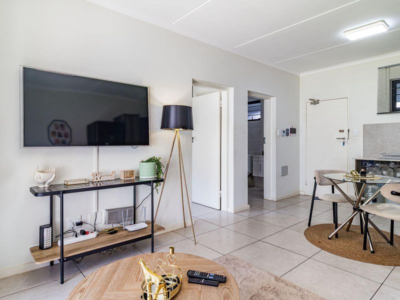 Open-plan living area featuring tiled flooring, a compact kitchen with built-in cabinetry, and direct access to adjacent rooms.