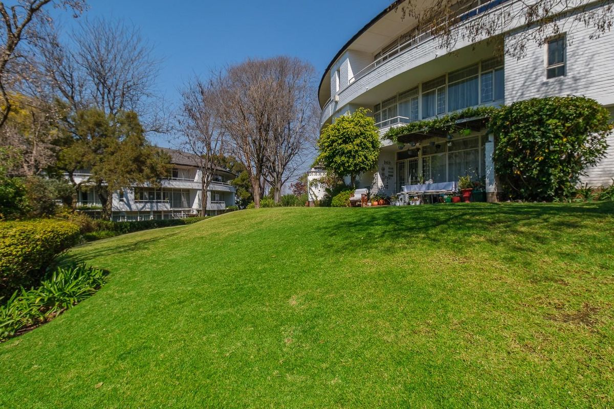 A view of the rear apartment building facade featuring tiered balconies and extensive landscaped garden grounds.