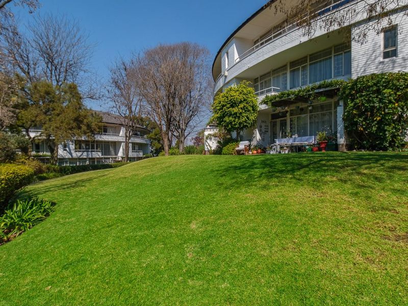 A view of the rear apartment building facade featuring tiered balconies and extensive landscaped garden grounds.
