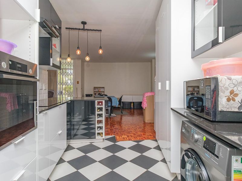Modern open-plan kitchen featuring high-gloss cabinetry, built-in appliances, and a stylish checkerboard floor, flowing into a living area with parquet flooring.