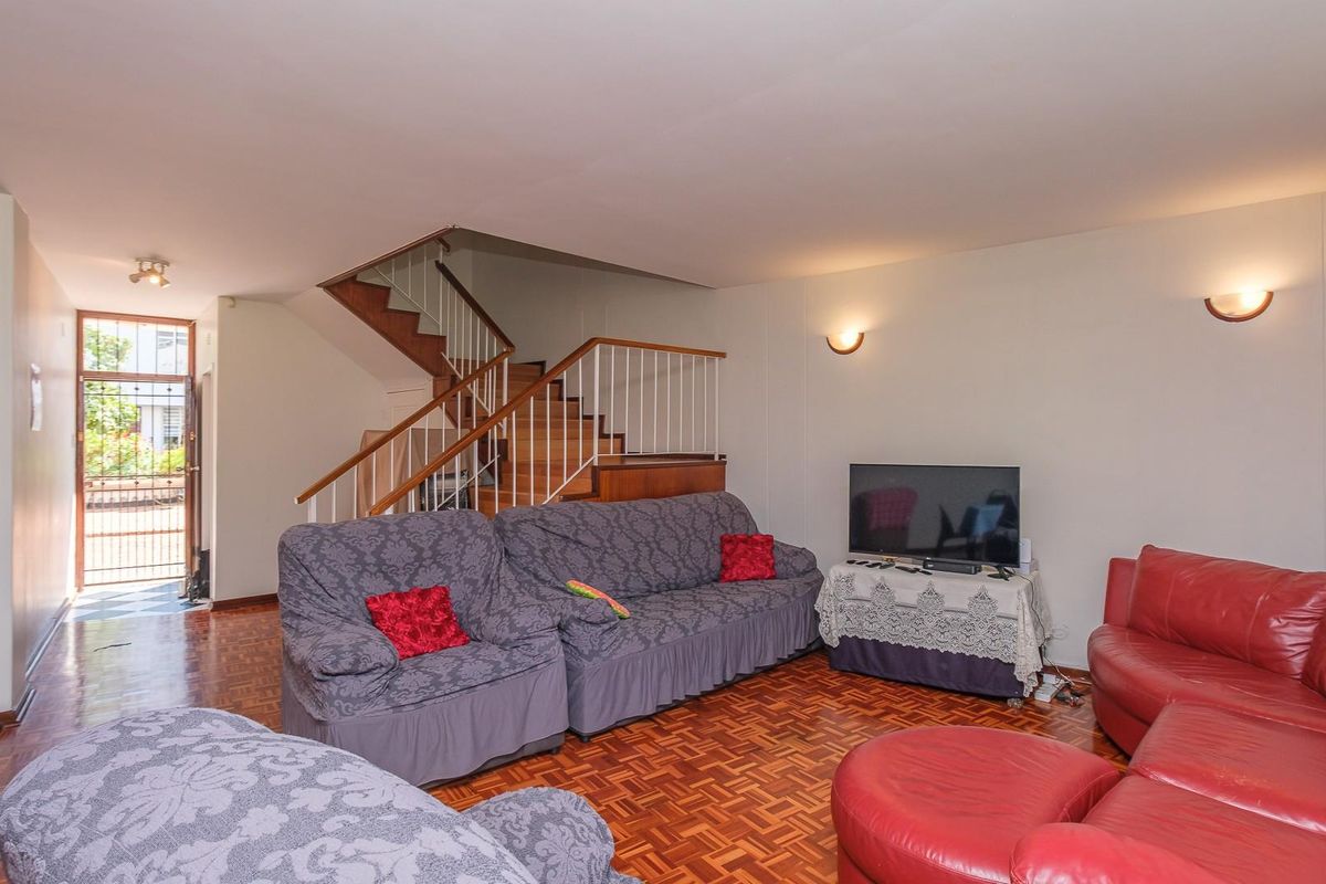 Spacious living room featuring traditional wooden parquet flooring and an open staircase with a metal balustrade, leading to the upper level.