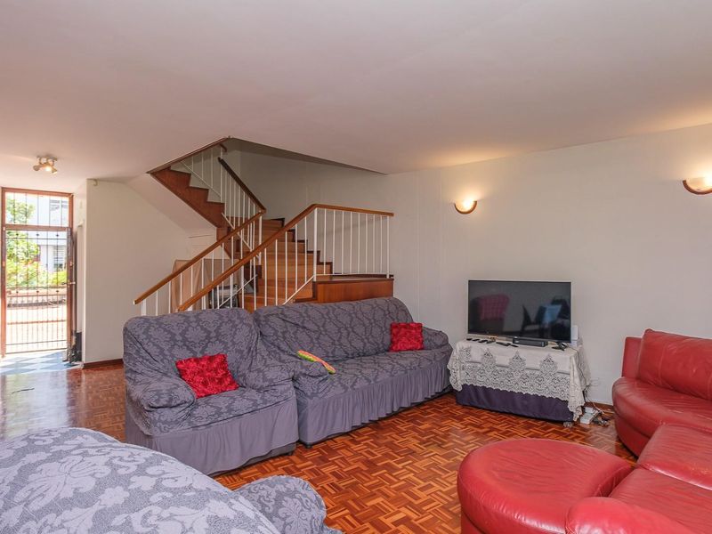 Spacious living room featuring traditional wooden parquet flooring and an open staircase with a metal balustrade, leading to the upper level.