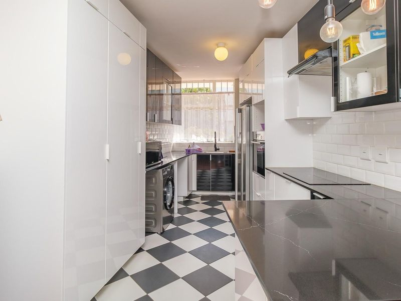 Modern kitchen featuring high-gloss cabinetry, stone countertops, subway tile backsplash, and a classic checkerboard tiled floor with integrated appliances.