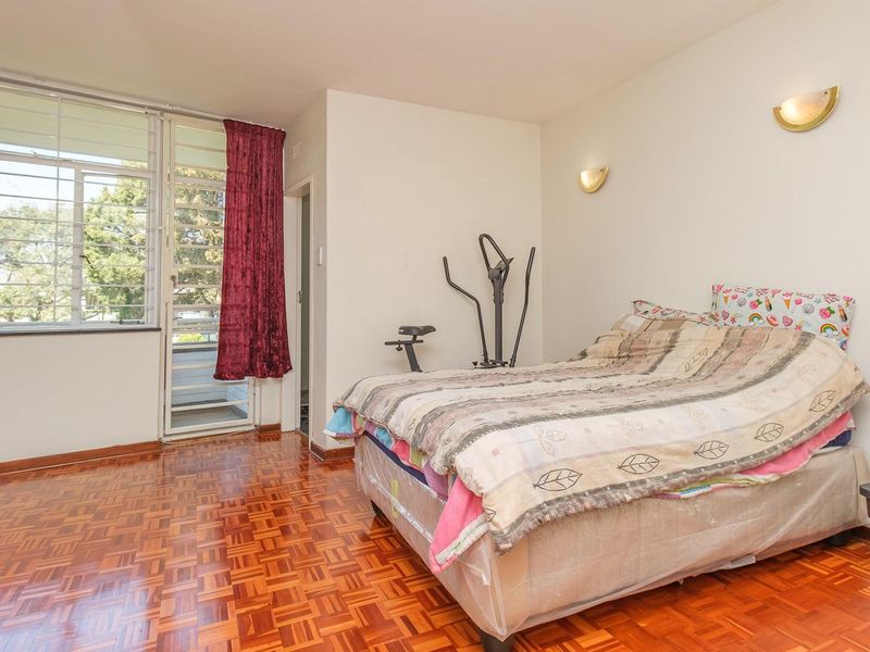 A bedroom featuring classic parquet flooring, wall-mounted lighting, and a sliding glass door providing access to an outdoor balcony area.