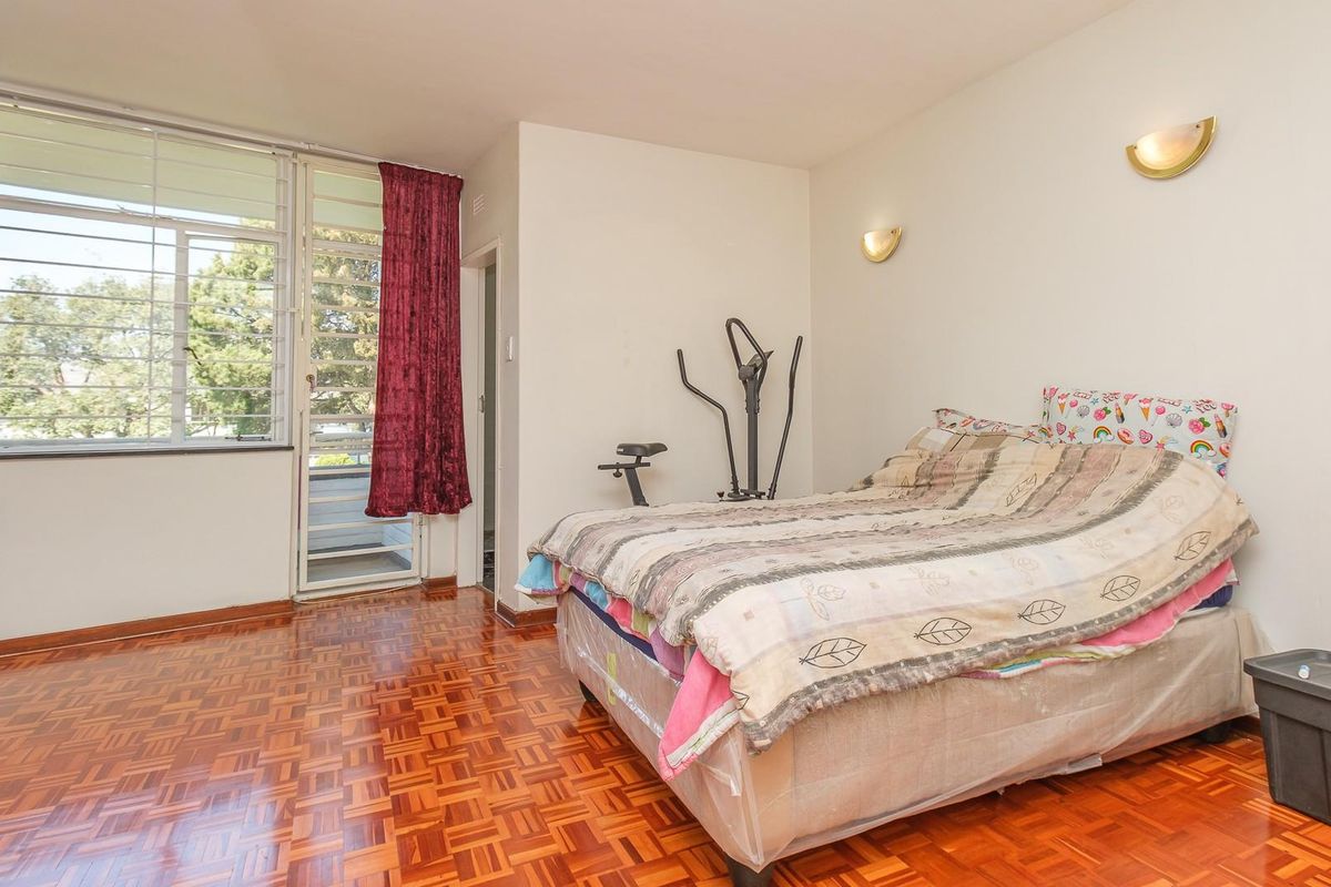 A bedroom featuring classic parquet flooring, wall-mounted lighting, and a sliding glass door providing access to an outdoor balcony area.