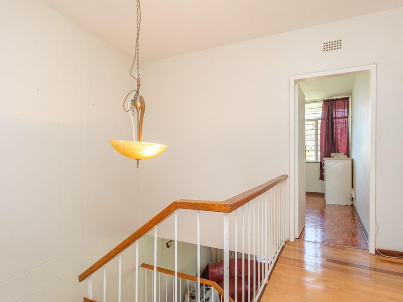 A bright hallway featuring a wooden staircase with a metal balustrade, parquet flooring, and a classic pendant light fixture.