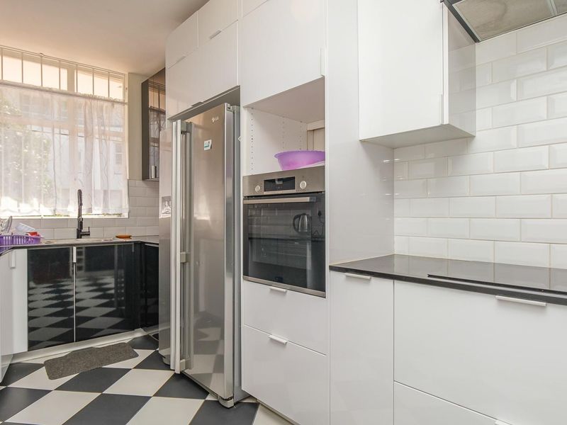 Modern kitchen featuring high-contrast black and white cabinetry, subway tile backsplash, built-in oven, and durable checkered flooring with ample storage space.