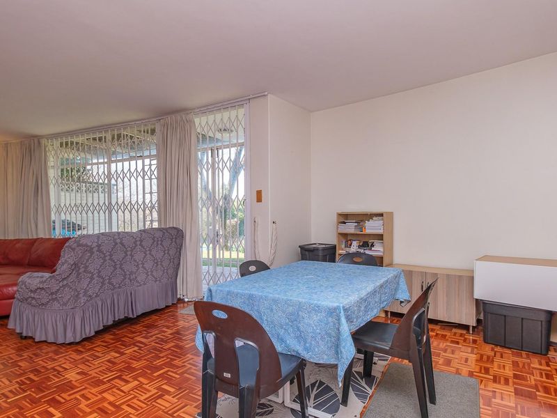 Spacious living area featuring classic parquet flooring, a wall sconce, and a sliding glass door with security gate leading to the exterior.