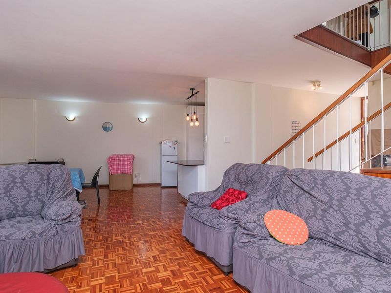 Open-plan living area featuring parquet flooring, a breakfast counter, and a staircase with a wooden handrail leading to the upper level.