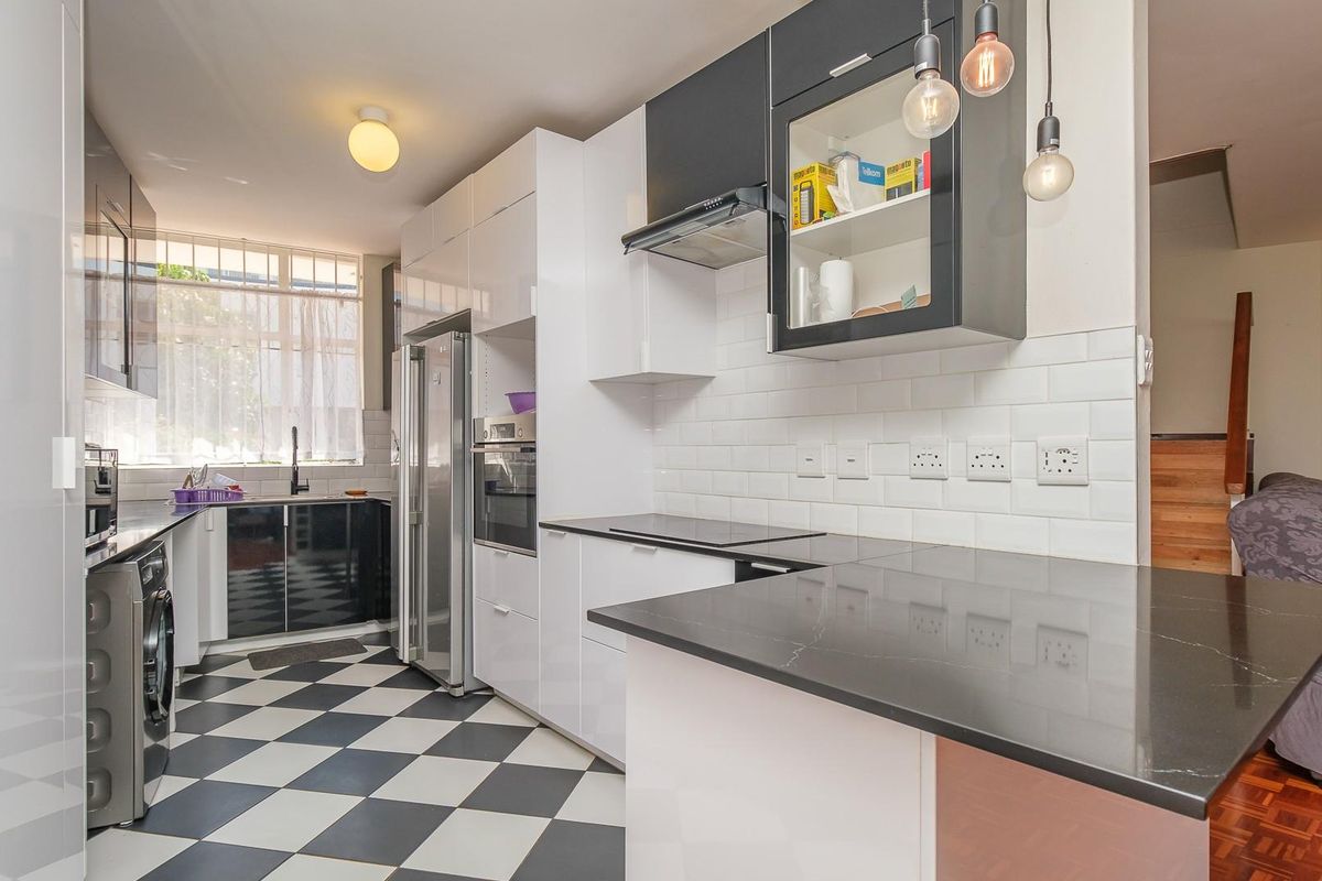 Modern kitchen featuring high-gloss cabinetry, stone countertops, subway tile backsplash, and integrated appliances with a distinctive checkerboard floor.