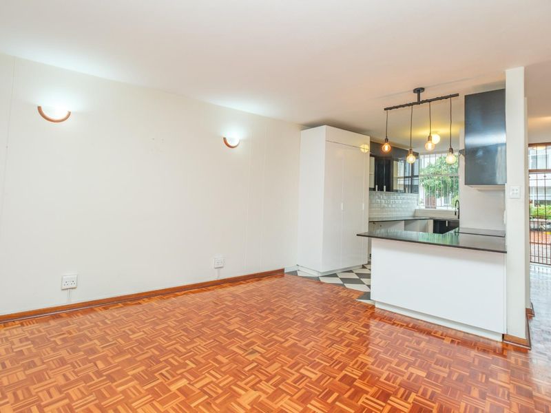 Open plan living area featuring parquet flooring, a modern kitchen with island, and stylish pendant lighting, creating a bright and functional space.