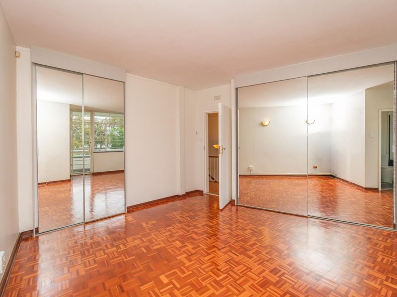 Spacious bedroom featuring classic parquet flooring and extensive built-in mirrored wardrobes, offering ample storage and a bright, open feel.