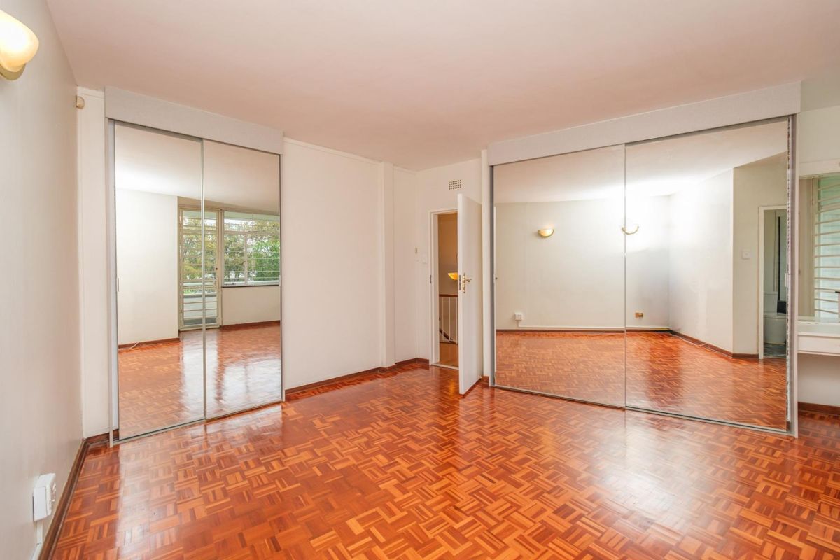 Spacious bedroom featuring classic parquet flooring and extensive built-in mirrored wardrobes, offering ample storage and a bright, open feel.