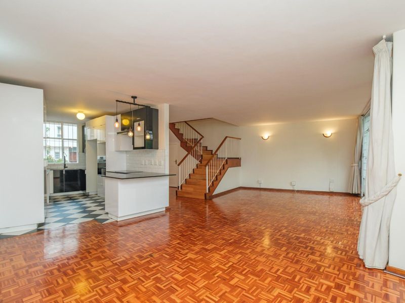 Spacious open-plan living area featuring parquet flooring, a modern kitchen with island, and a wooden staircase leading to the upper level.