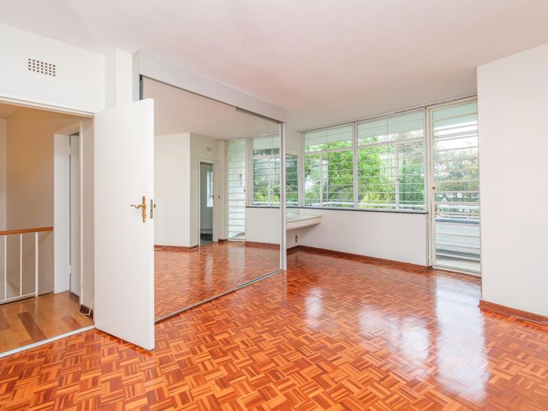 Spacious bedroom featuring classic parquet flooring, large windows providing natural light, and extensive mirrored built-in wardrobes with an integrated vanity area.