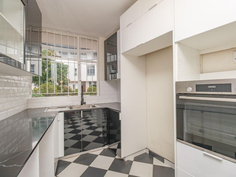 A compact kitchen featuring high-gloss cabinetry, black stone countertops, subway tile backsplash, and a built-in oven, with a classic black and white checkered floor.