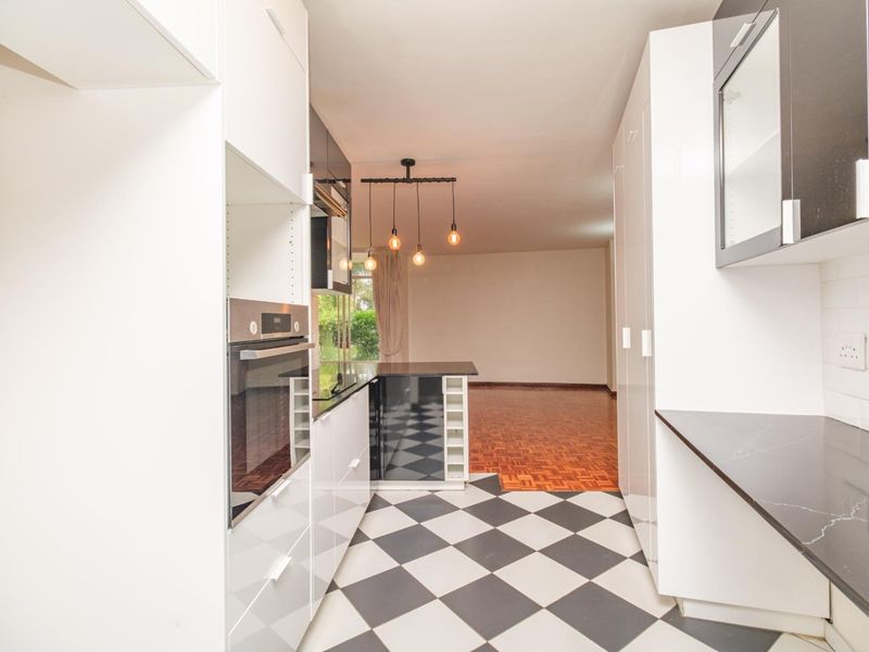 Modern kitchen featuring high-contrast black and white cabinetry, stone countertops, and a seamless transition to the adjacent living area with parquet flooring.