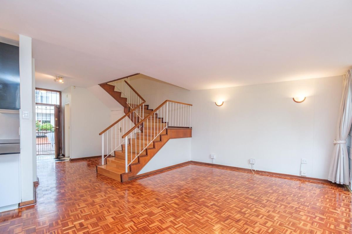 Spacious living area featuring classic parquet flooring and a central wooden staircase with a metal balustrade, leading to an open-plan layout.