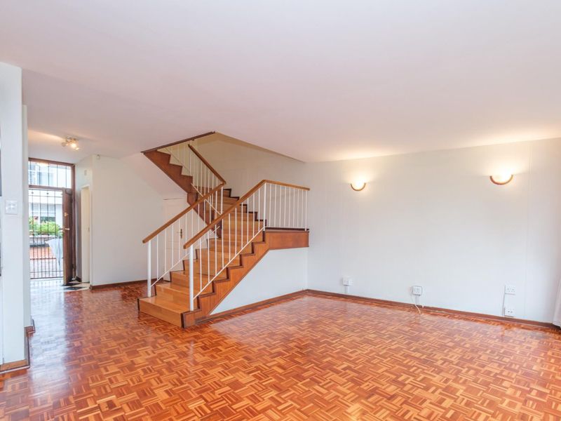 Spacious living area featuring classic parquet flooring and a central wooden staircase with a metal balustrade, leading to an open-plan layout.