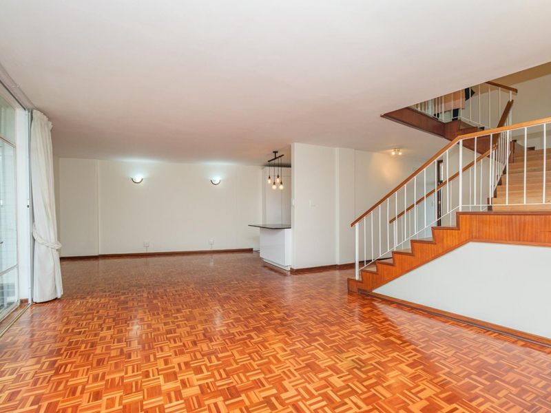 Spacious open-plan living area featuring classic parquet flooring, a wooden staircase with metal balustrade, and direct access to an outdoor space via sliding doors.
