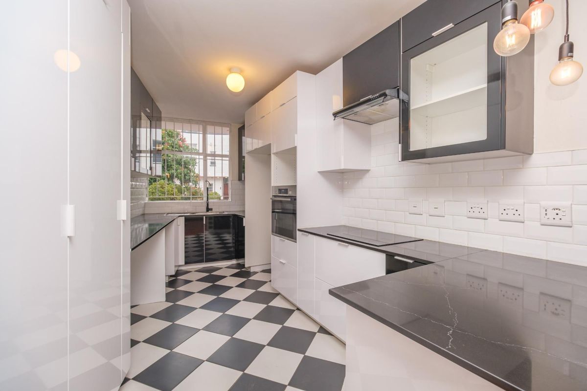 Modern kitchen featuring high-gloss cabinetry, stone countertops, subway tile backsplash, integrated oven, and a classic black and white checkered floor.