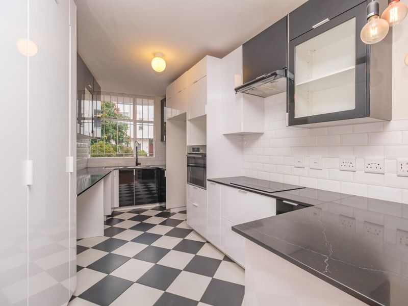 Modern kitchen featuring high-gloss cabinetry, stone countertops, subway tile backsplash, integrated oven, and a classic black and white checkered floor.