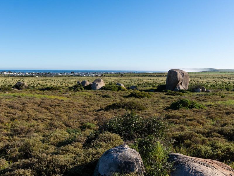 A scenic view of the natural landscape featuring large rock formations with a distant coastal town and ocean horizon in the background.