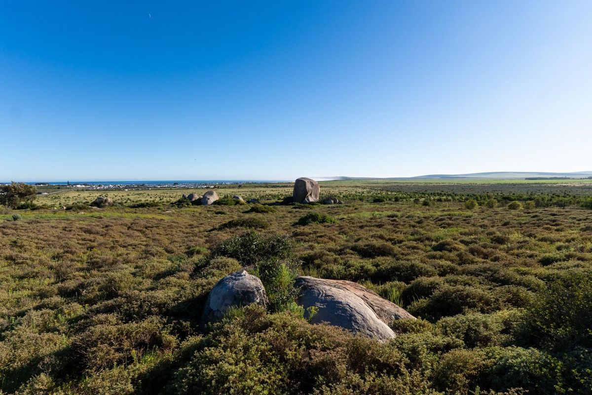 A wide-angle view of the vacant residential land, showcasing natural coastal vegetation, large rock formations, and distant ocean views.