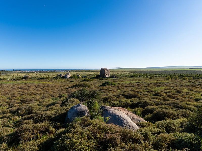 A wide-angle view of the vacant residential land, showcasing natural coastal vegetation, large rock formations, and distant ocean views.