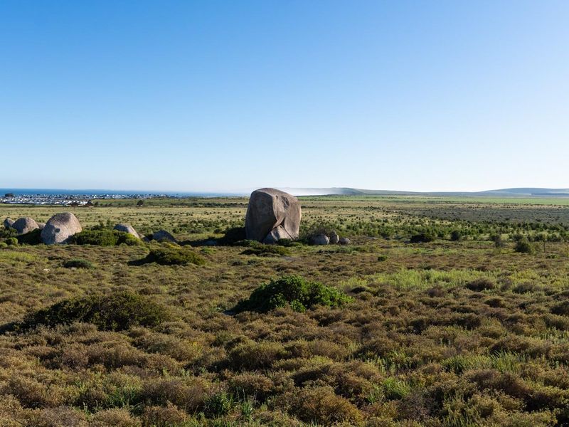 A wide-angle view of the vacant residential land featuring natural rock formations and distant coastal scenery.