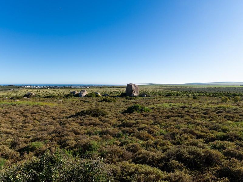A wide-angle view of the vacant residential land featuring natural coastal vegetation and large rock formations under a clear blue sky.