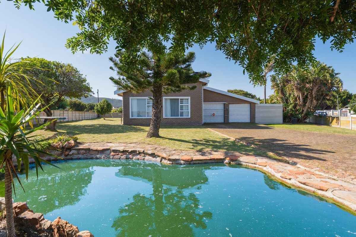 Rear view of a brick house featuring a swimming pool with stone coping, a large lawn, and a double garage with a paved driveway.
