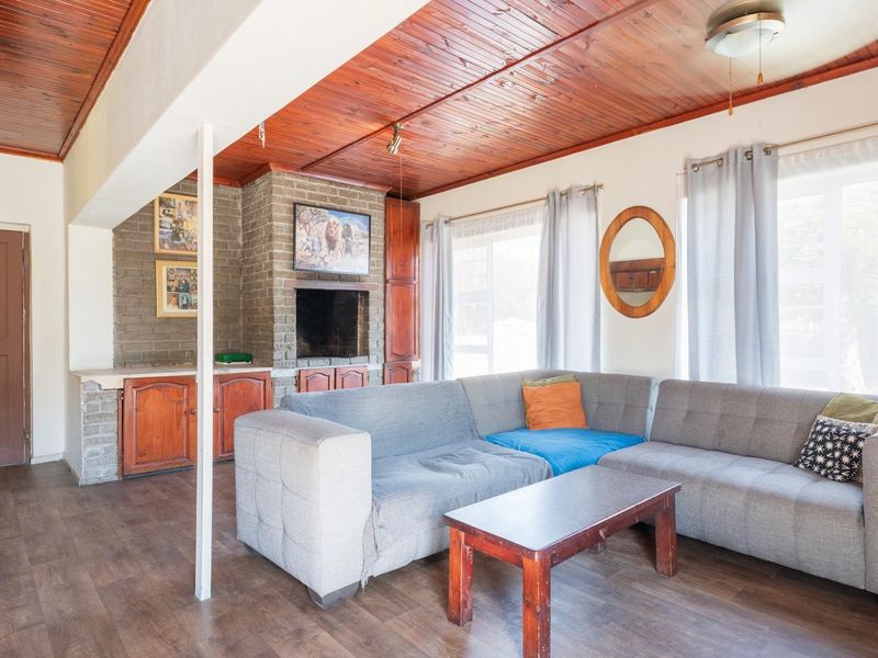 A living room featuring a brick fireplace, timber-clad ceiling, and laminate flooring, offering a rustic aesthetic with built-in storage cabinetry.