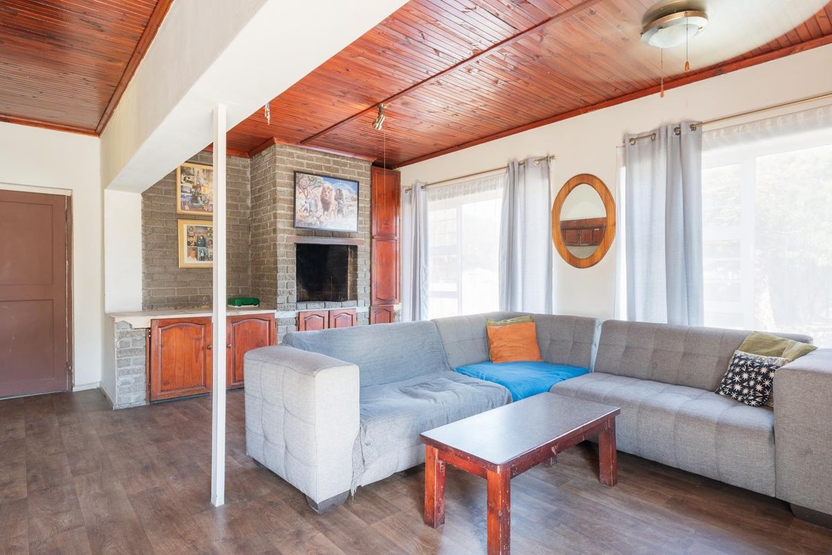 A living room featuring a brick fireplace, timber-clad ceiling, and laminate flooring, offering a rustic aesthetic with built-in storage cabinetry.