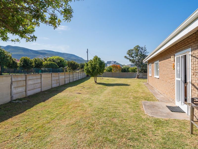 A spacious rear garden featuring a brick exterior wall, a concrete patio area, and a secure boundary wall with mountain views.