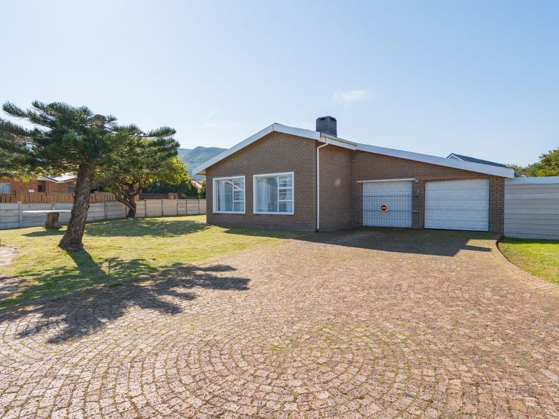 Front view of a brick house featuring a paved driveway, double garage, and a spacious front garden with a boundary wall.