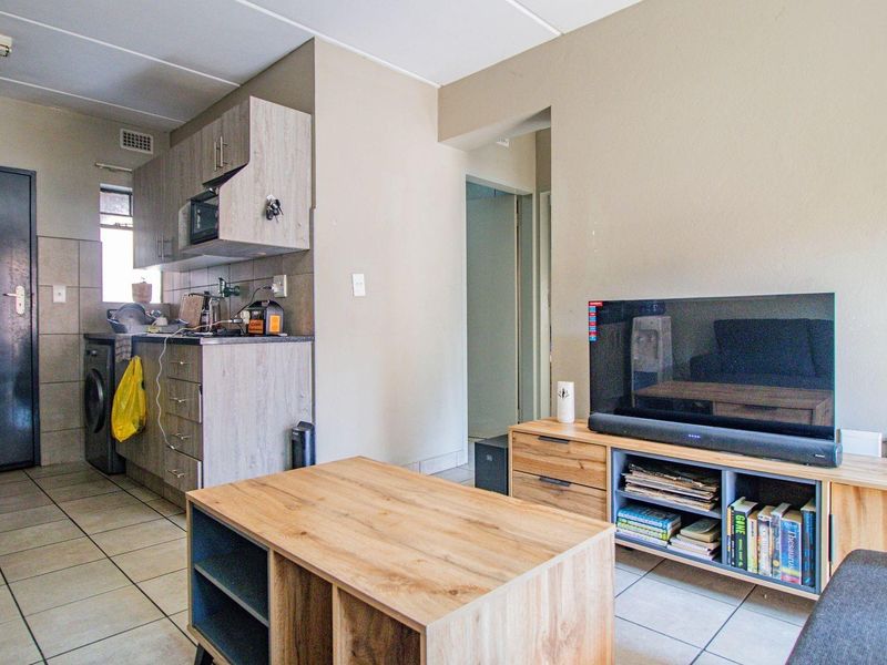 Open-plan living area featuring a compact kitchen with built-in cabinetry and tiled flooring, seamlessly flowing into the adjacent lounge space.
