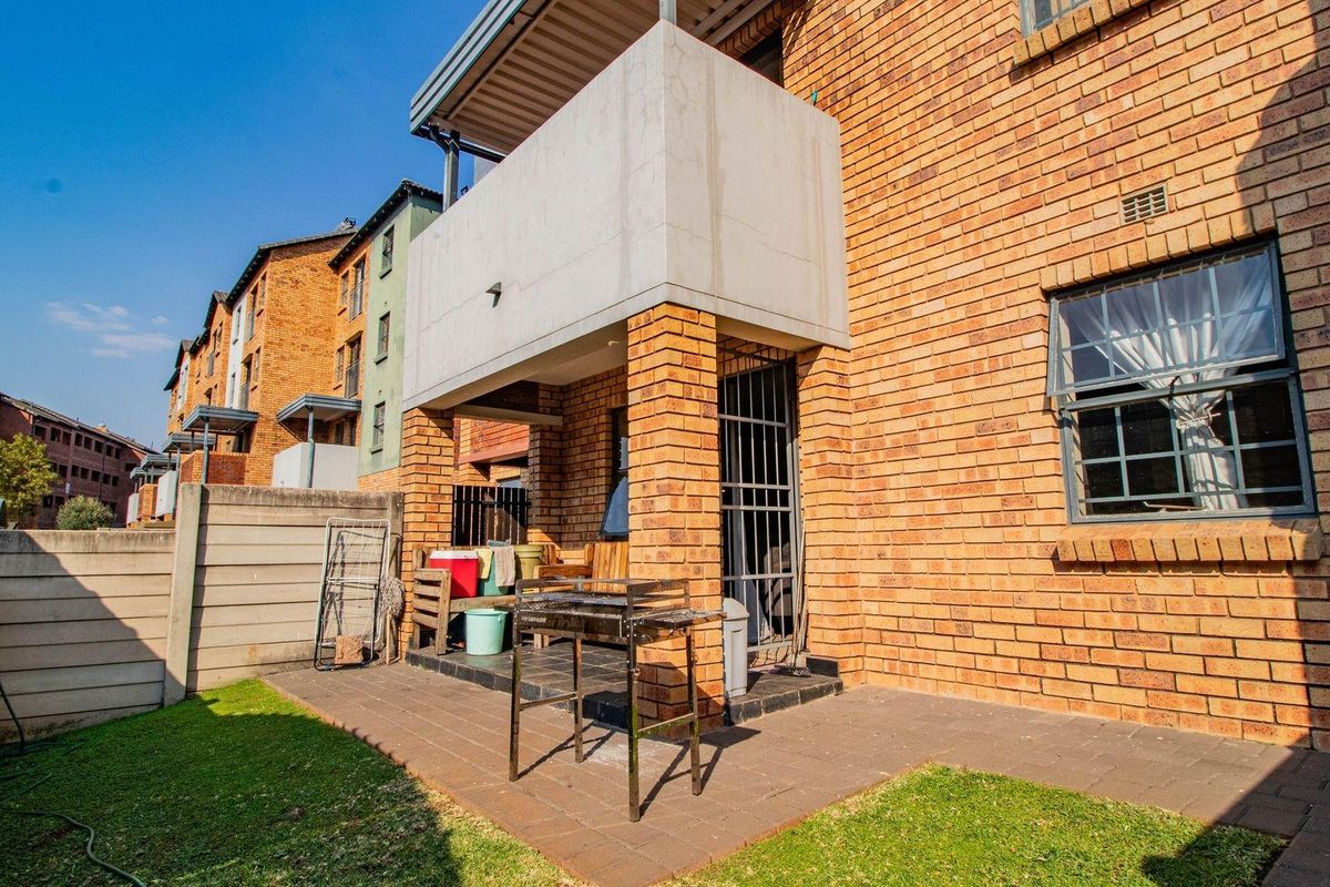 Rear view of the apartment featuring a brick facade, a covered patio area, and a small private garden space with a balcony above.