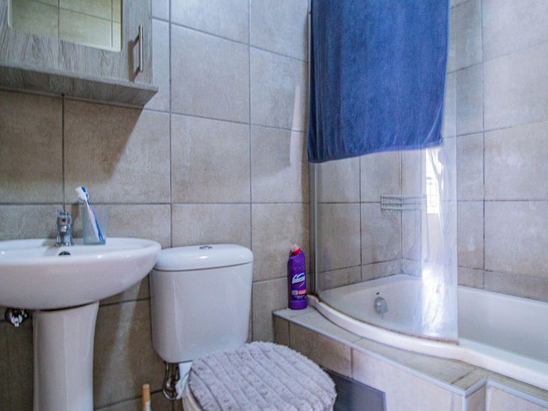 A functional bathroom featuring a pedestal basin, toilet, and a bathtub with a shower mixer, finished with neutral wall tiling.