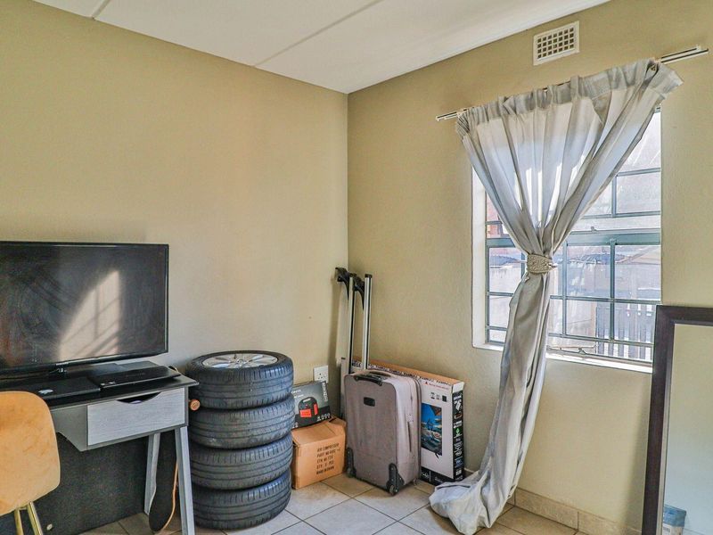 A bedroom featuring tiled flooring and a window fitted with security bars, providing natural light and ventilation.