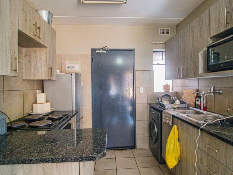 A functional kitchen featuring granite countertops, built-in cabinetry, an electric hob, and a built-in microwave with tiled flooring and backsplash.