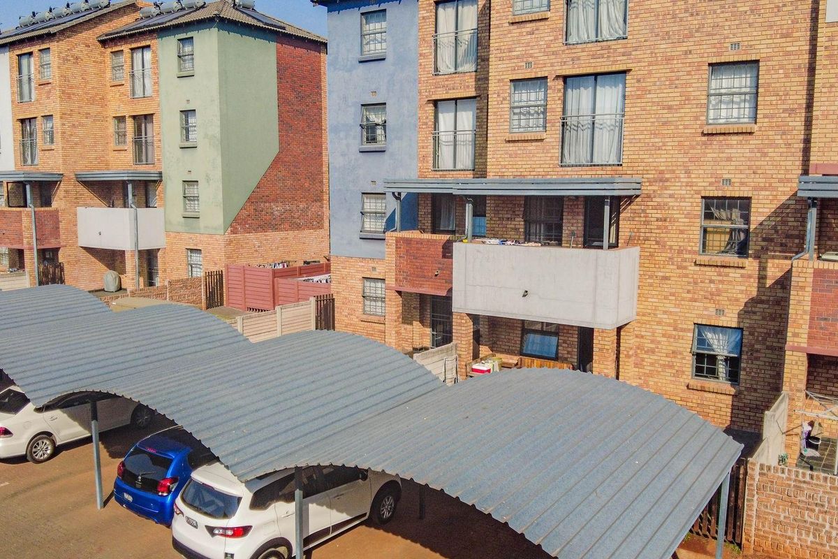 Aerial view of a multi-story brick apartment complex featuring covered parking bays and private balconies.