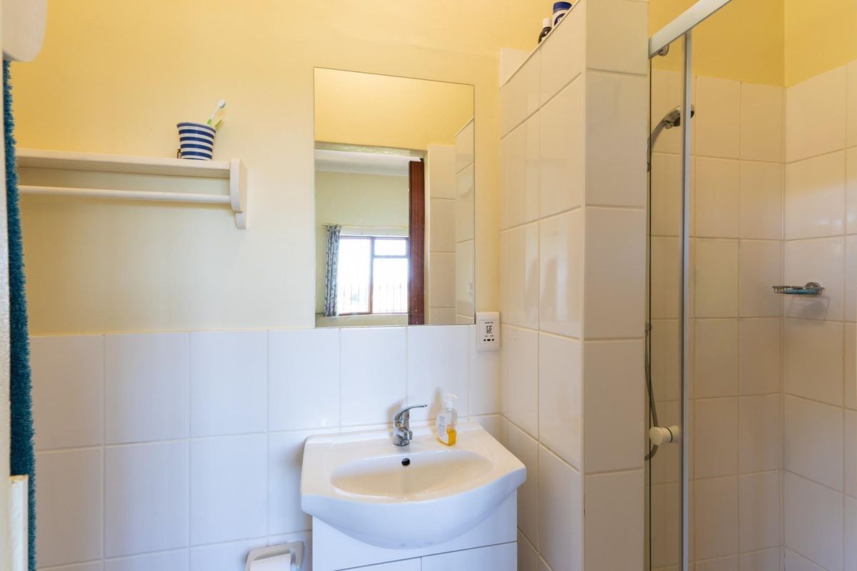 A functional bathroom featuring a wall-mounted basin, tiled splashback, and a glass-enclosed shower unit with neutral wall finishes.