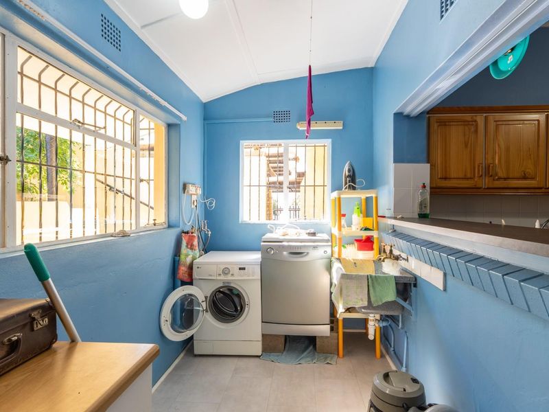 A functional laundry area featuring a built-in sink, tiled flooring, and security bars on the windows, providing a practical utility space.