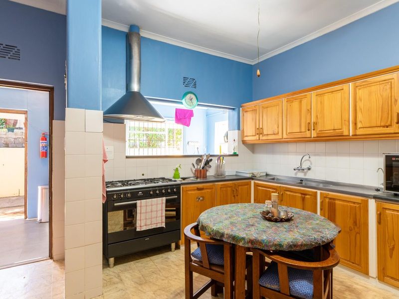 A functional kitchen featuring wooden cabinetry, a gas stove with extractor fan, tiled splashbacks, and direct access to an outdoor area.